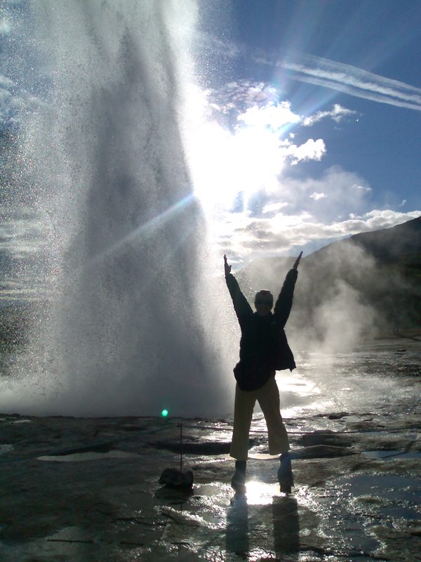 Silhouette with arms raised in front of an erupting geyser, Iceland