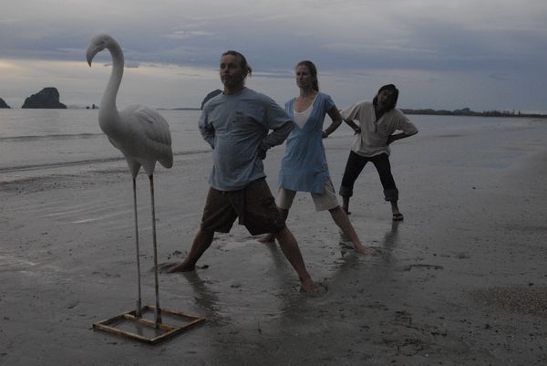Crew posing beside a flamingo lawn statue on the beach at dusk, Thailand