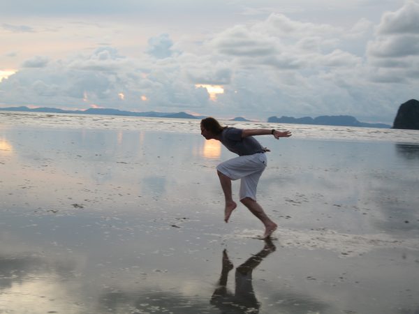 Man running across wet reflective sand at sunset, Thailand