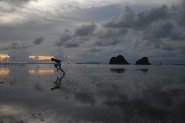 Man leaping across the tidal flats at sunset with karst islands in the distance, Thailand