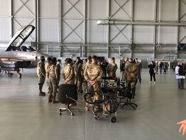 Airmen in formation briefing inside hangar with F-16 fighter jet, U.S. Air Force