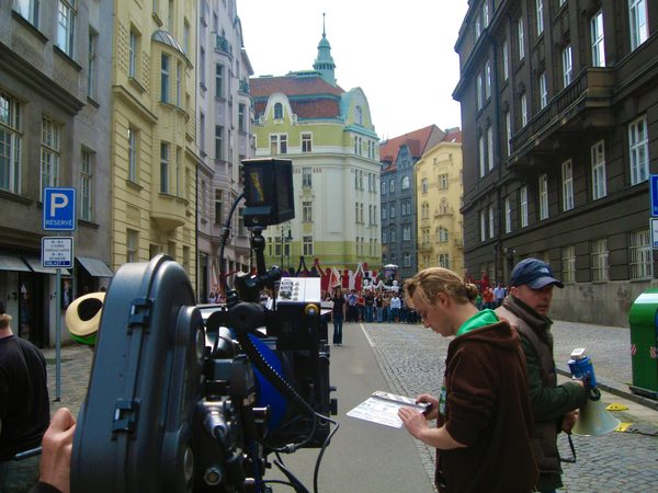 Camera crew filming a street scene with crowd and flags, Prague
