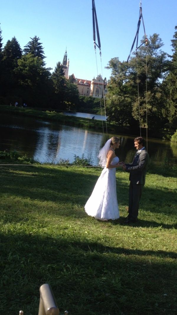 Bride and groom with wire rig overhead, castle and lake backdrop, Prague