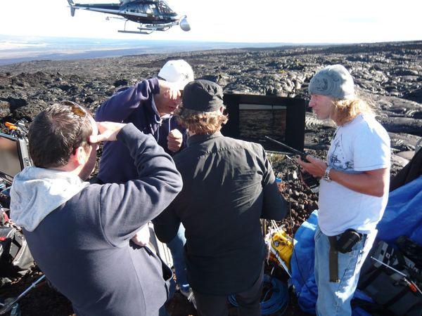 Crew huddle with helicopter overhead, lava fields, Hawaii