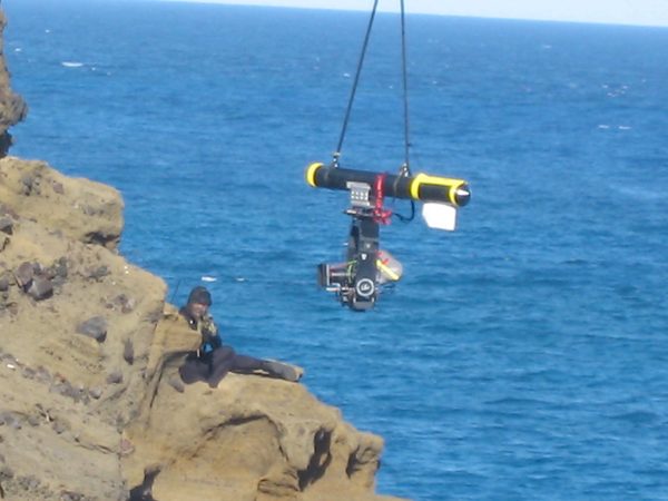 Camera crane rig suspended over ocean cliff edge, Hawaii